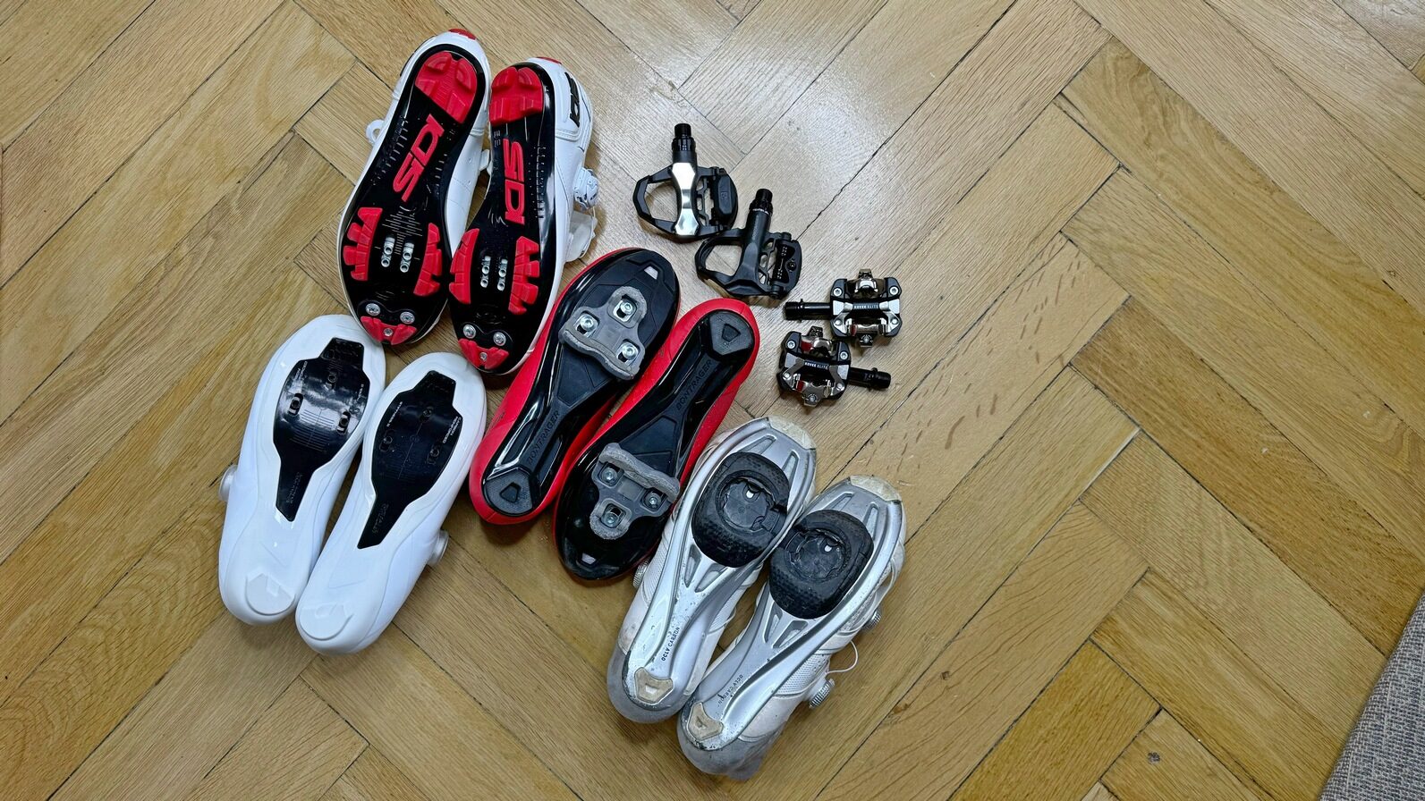 na zdjęciu widać kilka par butów rowerowych i cztery pary różnych typów pedałów nazywanych zatrzaskowymi - zdjęcie