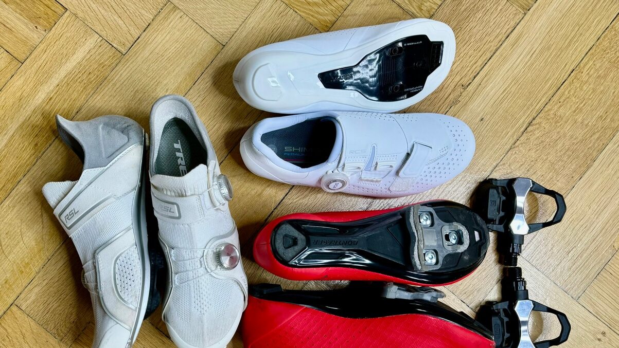 na zdjęciu widać trzy pary butów do uprawiania kolarstwa szosowego plus przeznaczone do nich szosowe pedały. Byty są białe i czerwone. 