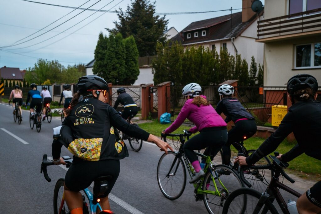 na zdjęciu widać grupę kobiet jadącą na rowerach szosowych, które uczą się jeździć w peletonie i widać też osobę zwaną Ministra Kolarstwa, która instruuje je w trakcie jazdy