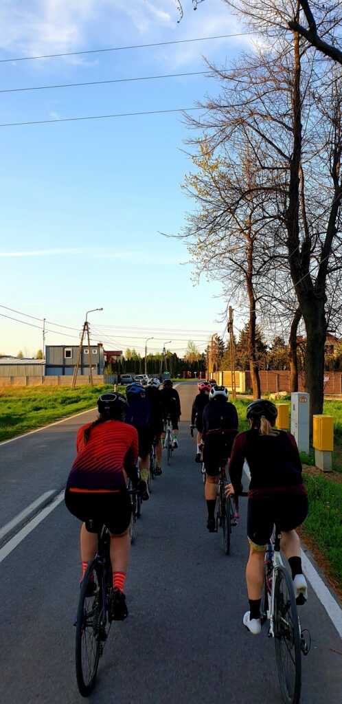 Na zdjęciu widać grupę kolarek szosowych jadących w ciasnym zwartym szyku na drodze