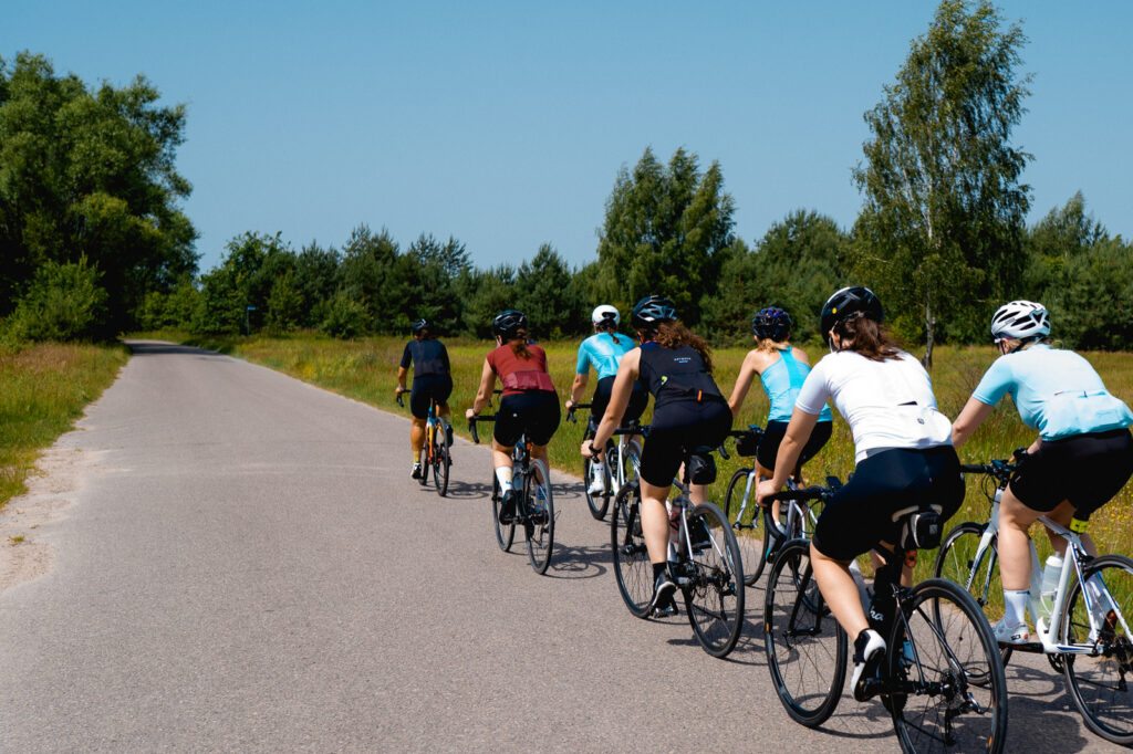 Na zdjęciu widać grupę kolarek szosowych jadących w ciasnym zwartym szyku jna drodze