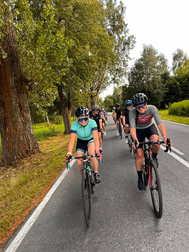 Na zdjęciu widać grupę kolarek szosowych jadących w ciasnym zwartym szyku jna drodze