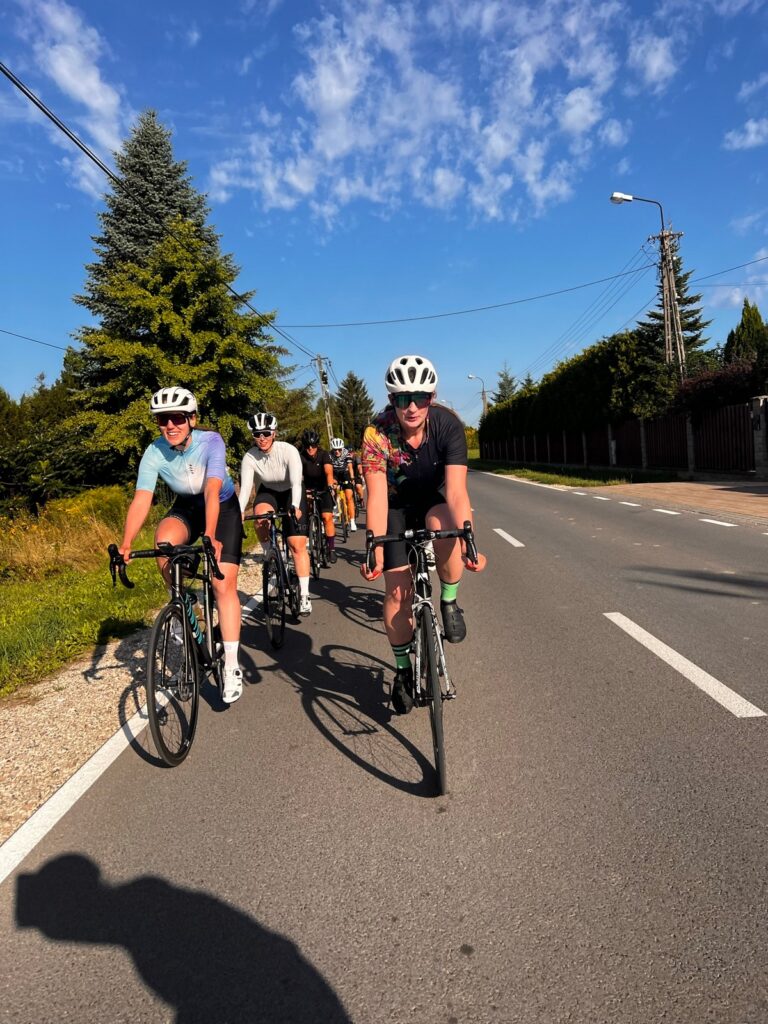Na zdjęciu widać grupę kolarek szosowych jadących w ciasnym zwartym szyku jna drodze