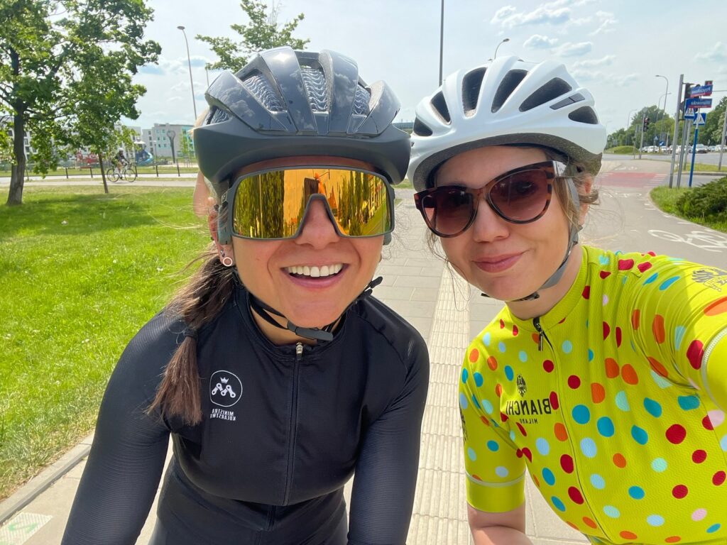 na zdjęciu są dwie kolarki ubrane w kaski i ubrania kolarskie, jedna z nich jest kursantką na szkoleniu na rowerze szosowym podczas szkolenia indywidualnego u Ministry Kolarstwa