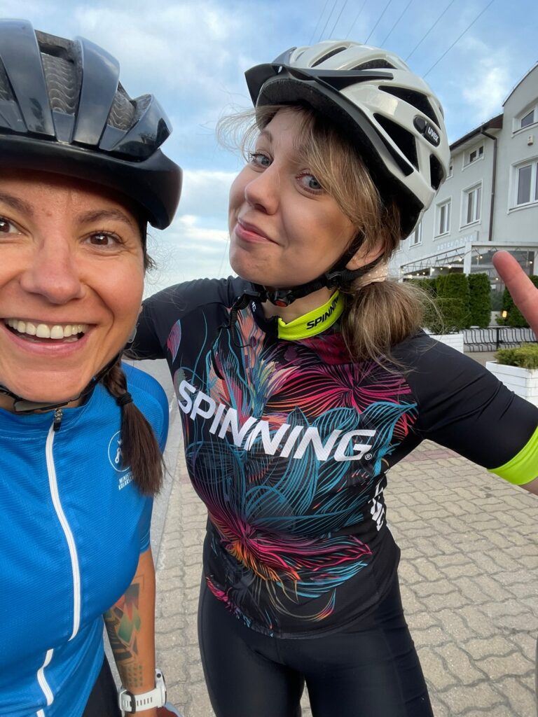 na zdjęciu są dwie kolarki ubrane w kaski i ubrania kolarskie, jedna z nich jest kursantką na szkoleniu na rowerze szosowym podczas szkolenia indywidualnego u Ministry Kolarstwa