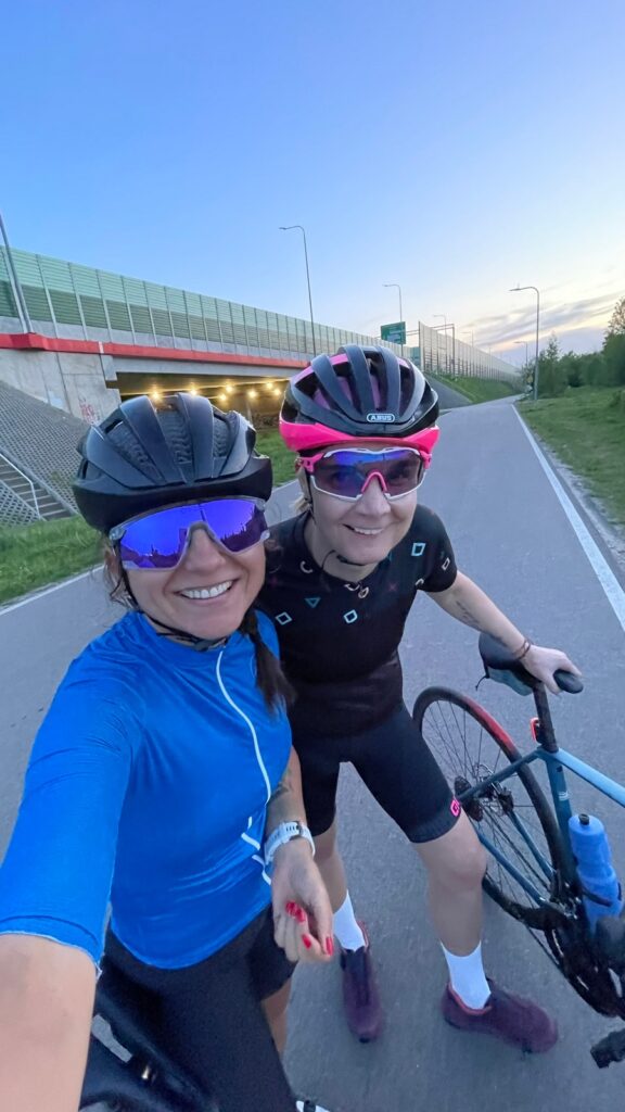 na zdjęciu są dwie kolarki ubrane w kaski i ubrania kolarskie, jedna z nich jest kursantką na szkoleniu na rowerze szosowym podczas szkolenia indywidualnego u Ministry Kolarstwa