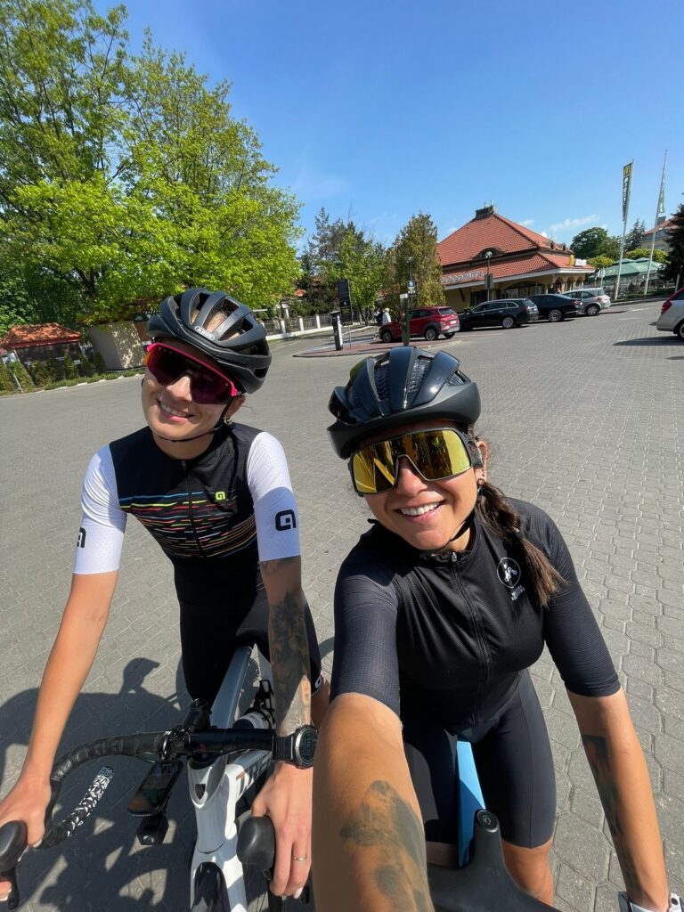 na zdjęciu są dwie kolarki ubrane w kaski i ubrania kolarskie, jedna z nich jest kursantką na szkoleniu na rowerze szosowym podczas szkolenia indywidualnego u Ministry Kolarstwa