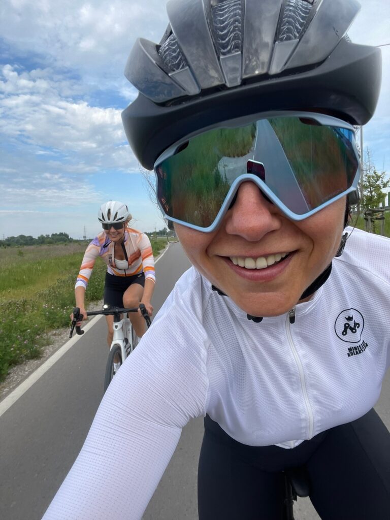 na zdjęciu są dwie kolarki ubrane w kaski i ubrania kolarskie, jedna z nich jest kursantką na szkoleniu na rowerze szosowym podczas szkolenia indywidualnego u Ministry Kolarstwa